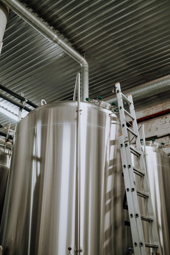 pexels-photo-5532836-5532836 Vertical view of stainless steel fermenter tanks with a metal ladder in a brewery.
