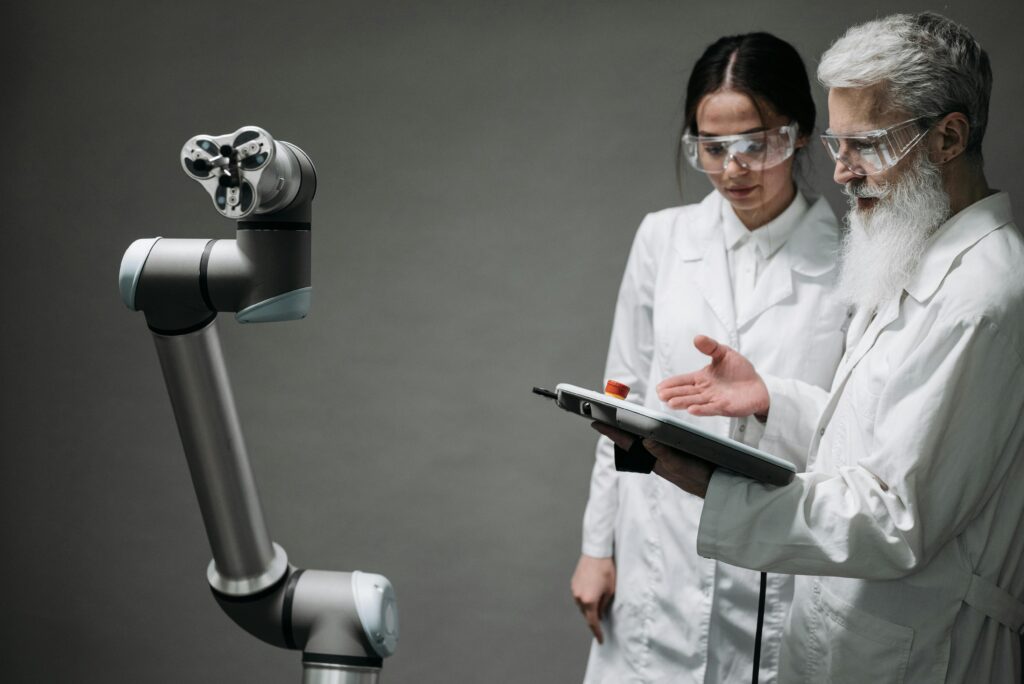 pexels-photo-8438994-8438994 Researchers in lab coats and safety glasses engaging with a robotic arm in a lab setting.