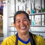 Happy Thai woman smiling brightly at an outdoor bar in Thailand, capturing a moment of joy.